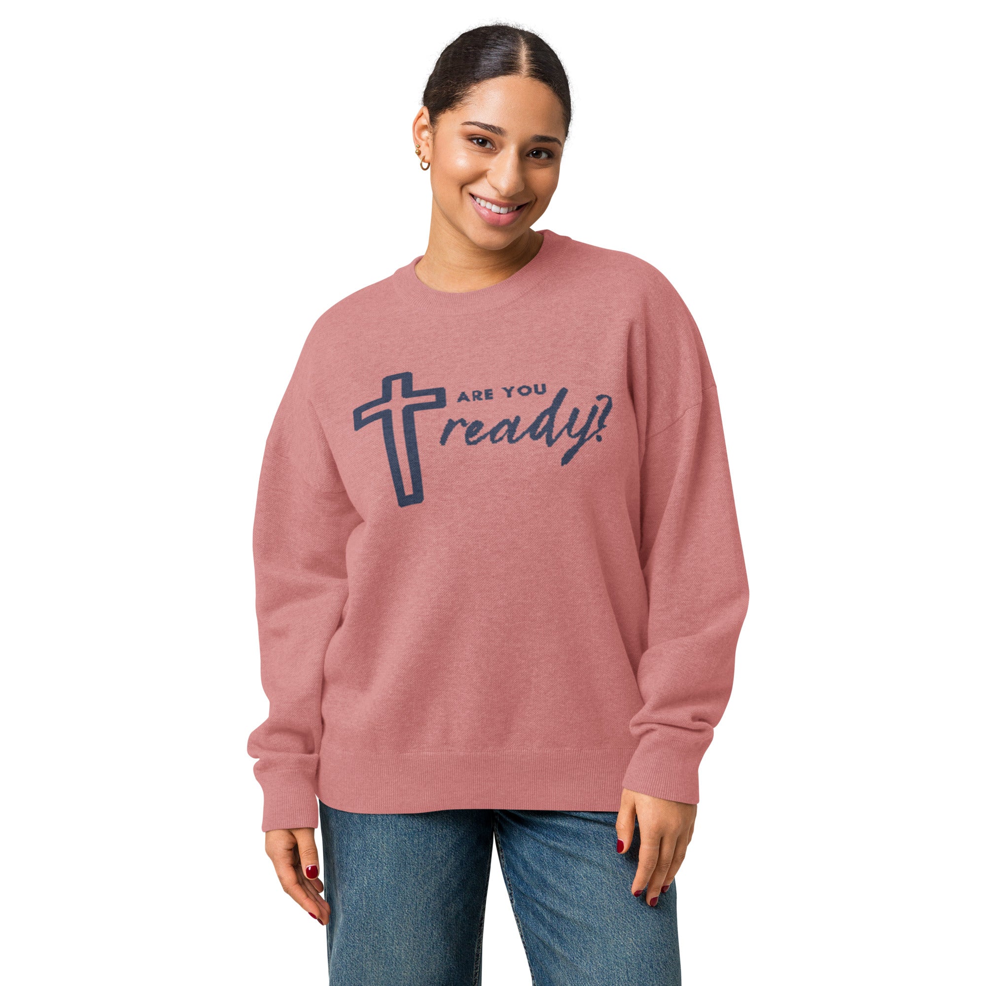 Front of woman wearing pink knitted sweater with image of cross and text in navy blue, standing looking at camera smiling