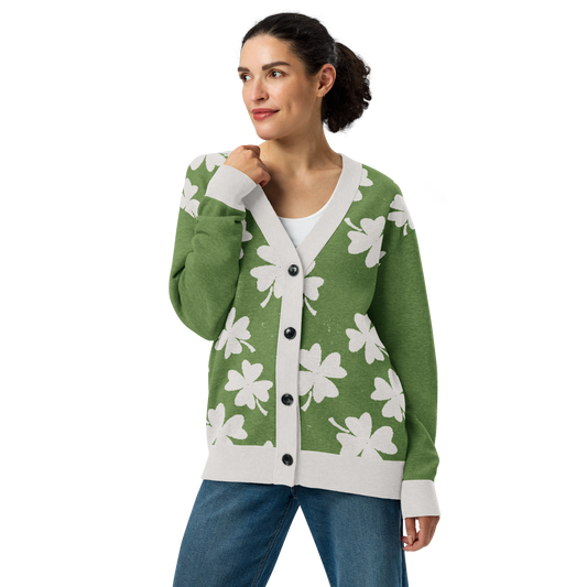 Front of Woman wearing a distressed green cardigan with white four-leaf clover pattern, buttoned up, looking to the right with arm bent upward 