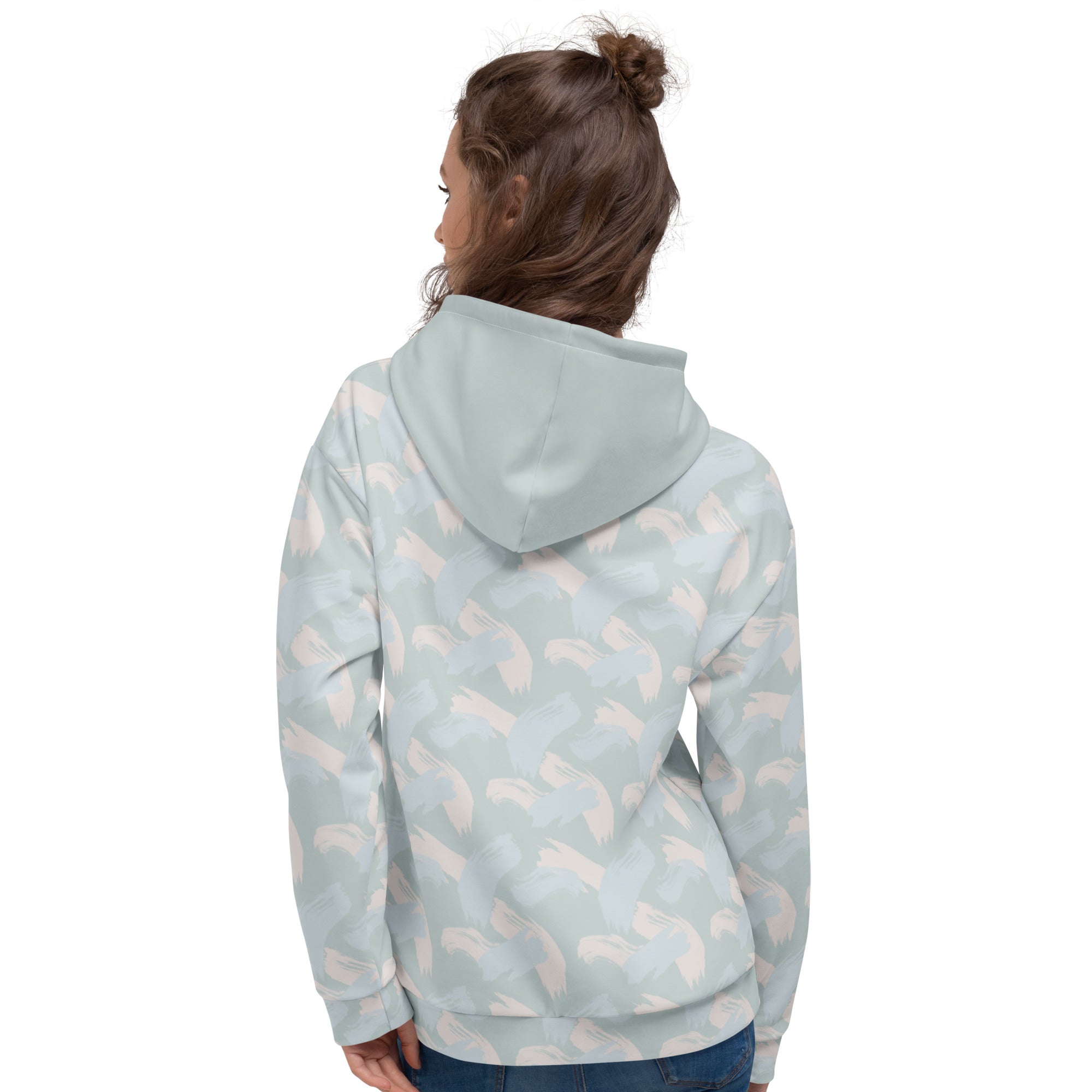 Back of woman wearing a light blue hoodie with abstract pattern of paint strokes in multiple colors and solid hood looking left 