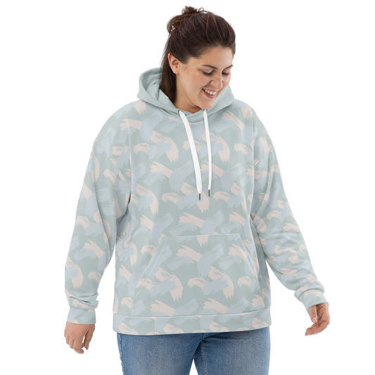 Front of Woman wearing a light blue hoodie with abstract pattern of paint strokes in multiple colors and solid hood with pull strings hanging while looking down and smiling 